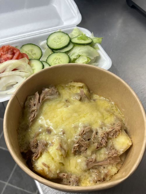 A cheese and tuna jacket potato in a takeaway bowl, with a side of salad.